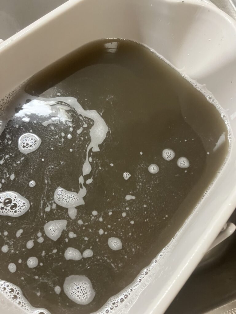 油汚れでベトベトなレンジフードの分解したファンを専用の薬剤を入れたバケツに付けたときの汚水